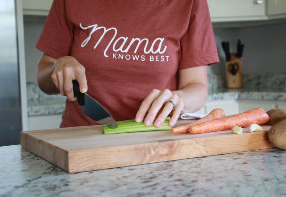 Woman in kitchen cutting vegetables on cutting board for menu plan of what to make for supper.