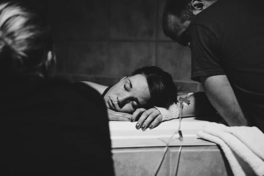 Woman resting in labor tub with the support of her doula and husband