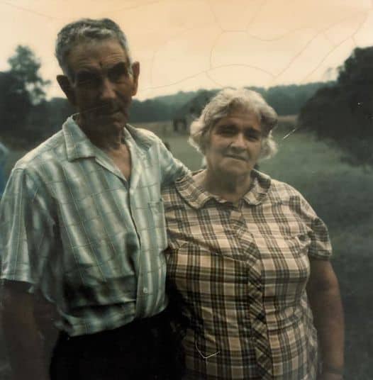 Old photo of grandma and grandpa together in front of field.