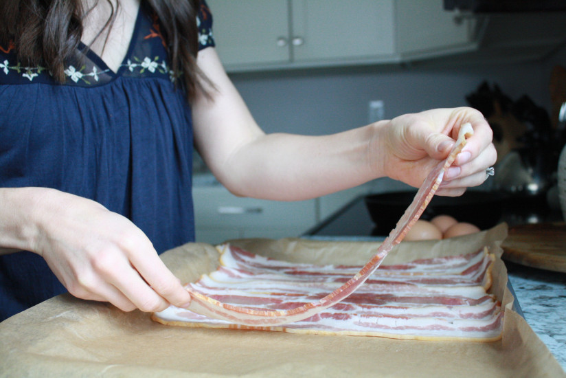 Woman in kitchen laying out bacon on a baking sheet that is covered with unbleached parchment paper for the best way to cook bacon.