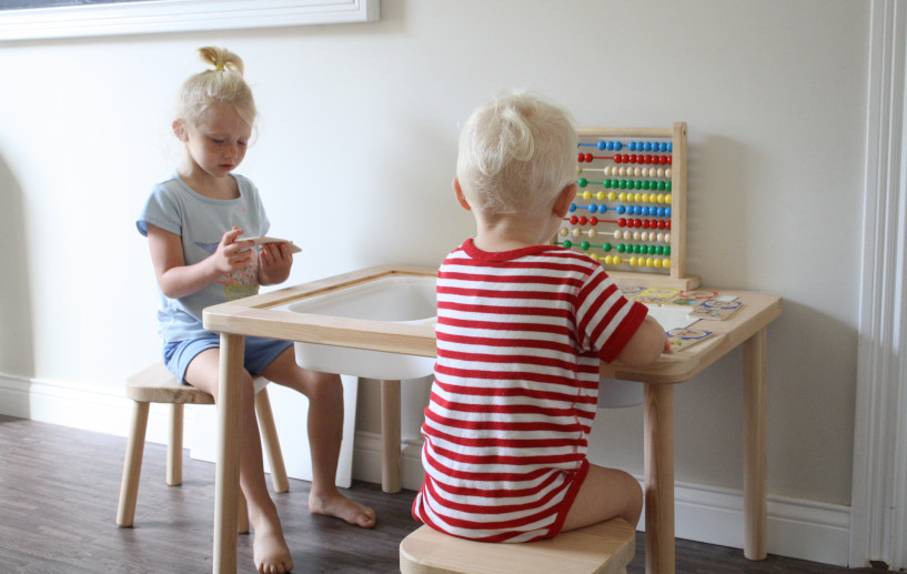 Two younger siblings, one girl, and one boy, at a sensory table playing with wooden puzzles. Method and advice for homeschooling with younger siblings.
