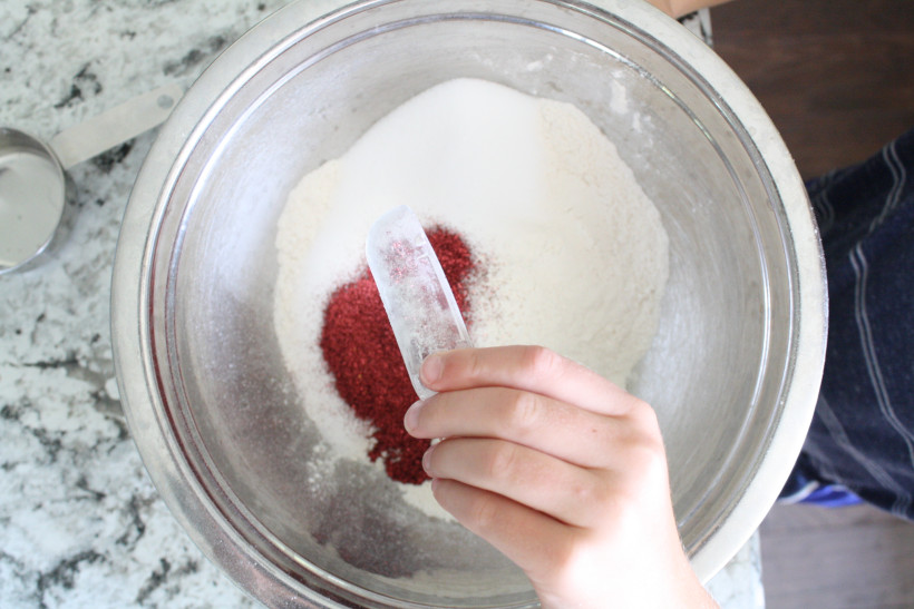 Child pouring glitter into flour and salt mixture in metal bowl.