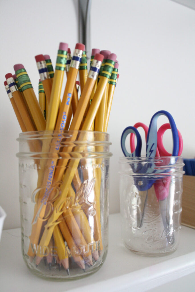 Up close of mason jar full of pencils and a smaller mason jar with scissors to organize your homeschool room.