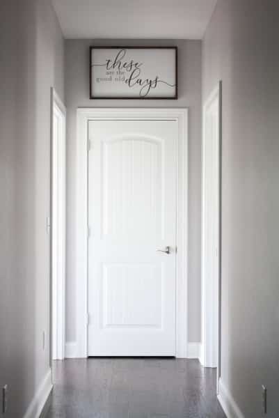 Long hallway with blank light gray walls. Wood hand painted sign at the end that says, 