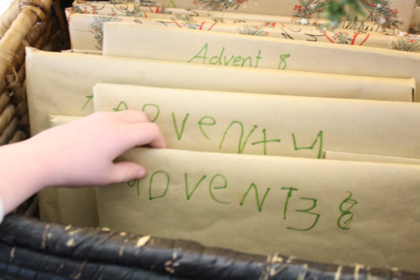 Child's hand reaching for a wrapped Advent book from a basket for Christmas traditions for kids.