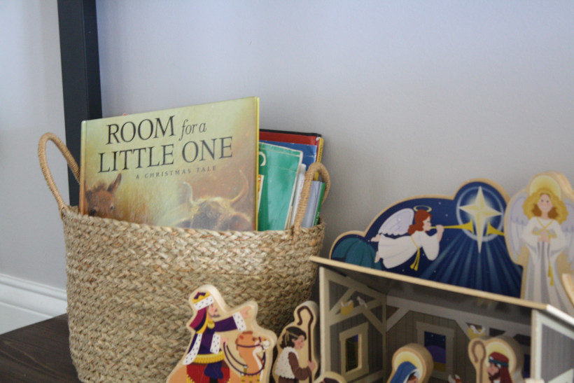 Books displayed in basket on shelf next to Nativity for Christmas books for kids.