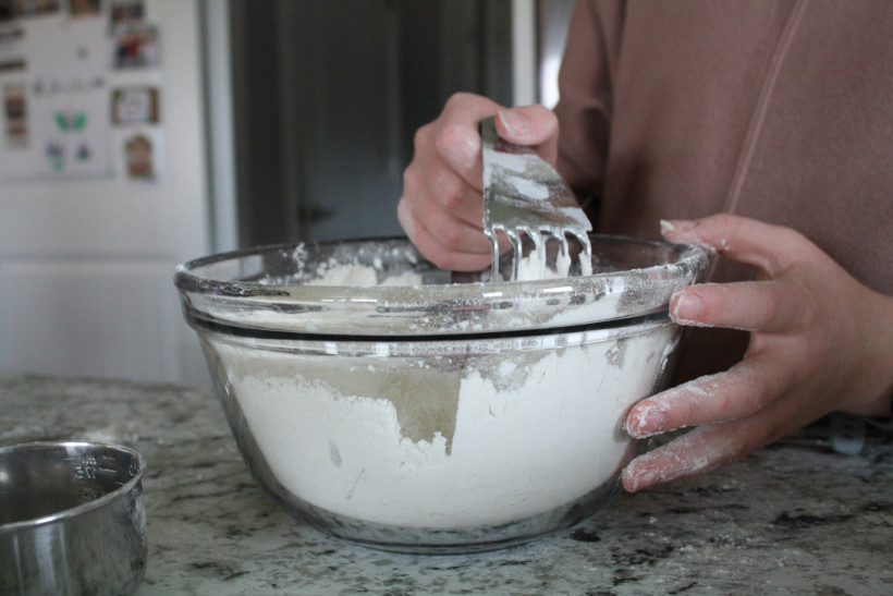 Woman using pastry cutter in glass bowl with flour to cut butter into the flour.