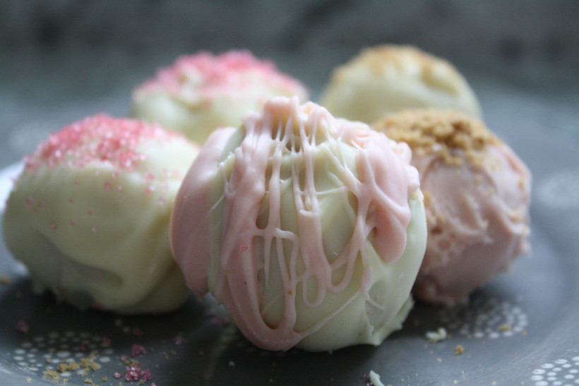 Completed variations of cheesecake balls recipe no bake. White chocolate cheesecake ball with pink colored white chocolate drizzled on top.