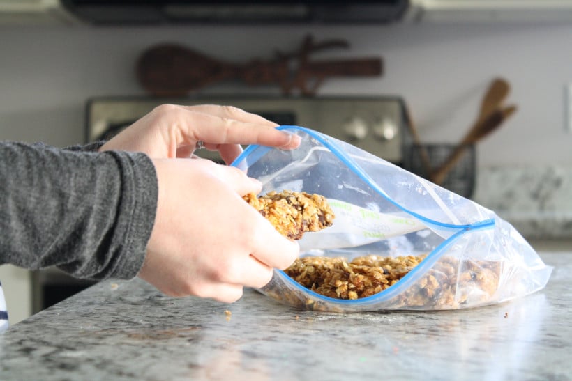 Woman placing chocolate chip granola bars inside of freezer bag to freeze.