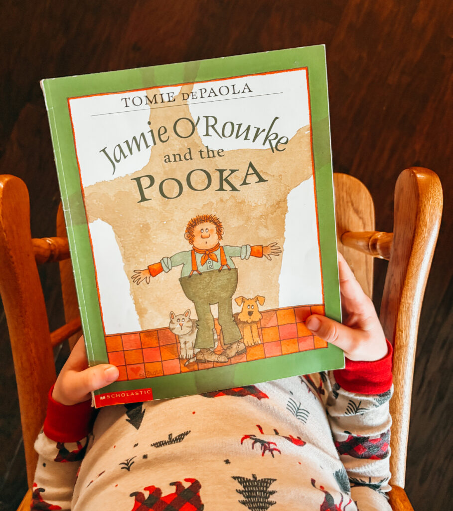 Child sitting in rocking chair with pajamas on holding the book Jamie O'Rourke and the Pooka.
