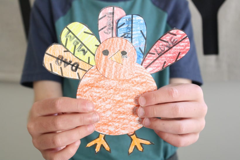 Child is holding a completed thankful turkey craft. 