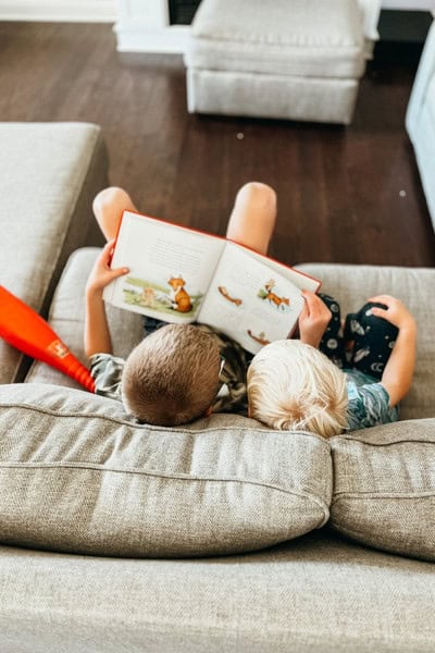 Above view of 2 boys reading a book together on the couch for one of the screen-free summer ideas.