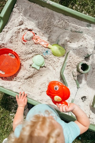 Showing summer routine for kids and mom with toddler playing in a sandbox outside. 
